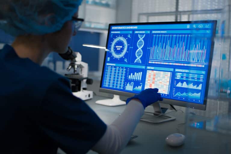 Female scientist in protective clothes and glasses looking at the computer screen. Researching genetic diseases and DNA test results