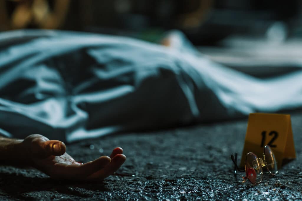 Cold Toned Picture: A Corpse Lying on the Floor and Covered. Victim's Hand is Peeking Out. Accidental Manslaughter Leaving Young Man for Dead. Glasses and Blood Marked as Evidence Next to the Corpse